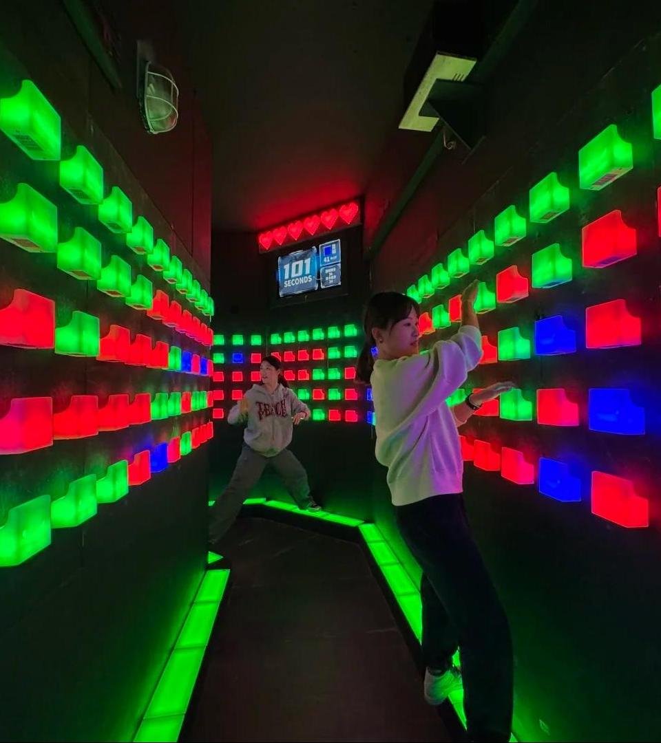 Two players stand on the steps, holding green blocks, and press blue blocks while avoiding red blocks.