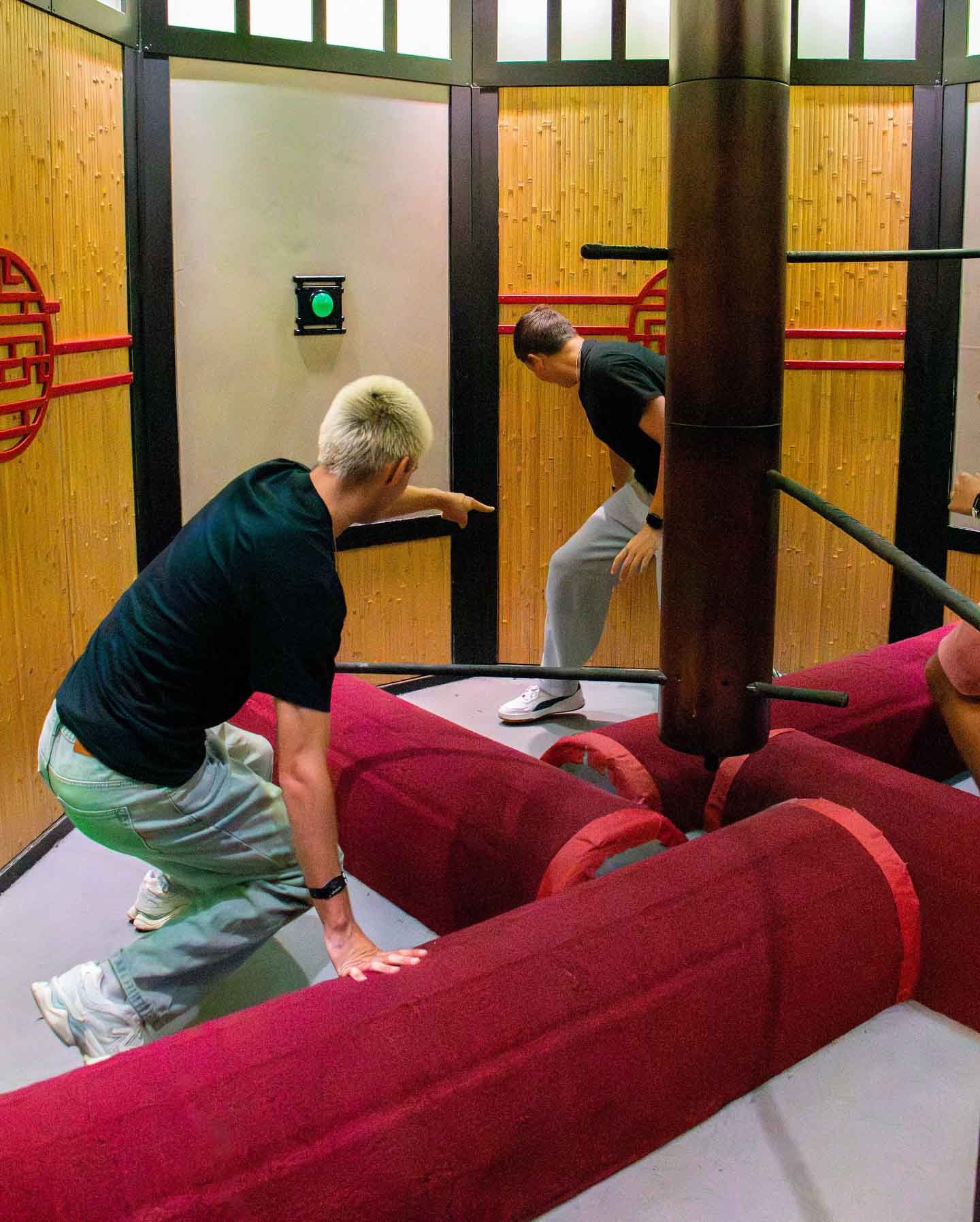 Mehrere Spieler spielen Rotating Obstacle Challenge und weichen den rotierenden Gummibalken aus, während sie Wandtasten drücken.