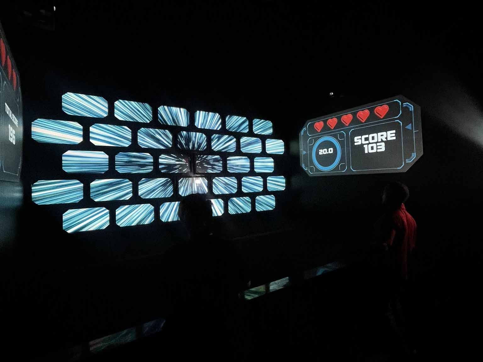 Spielszene Meteor Smash mit Spielern, die Bälle auf LED-Zielbildschirme werfen; seitliche Bildschirme zeigen Leben und Punktzahl an.