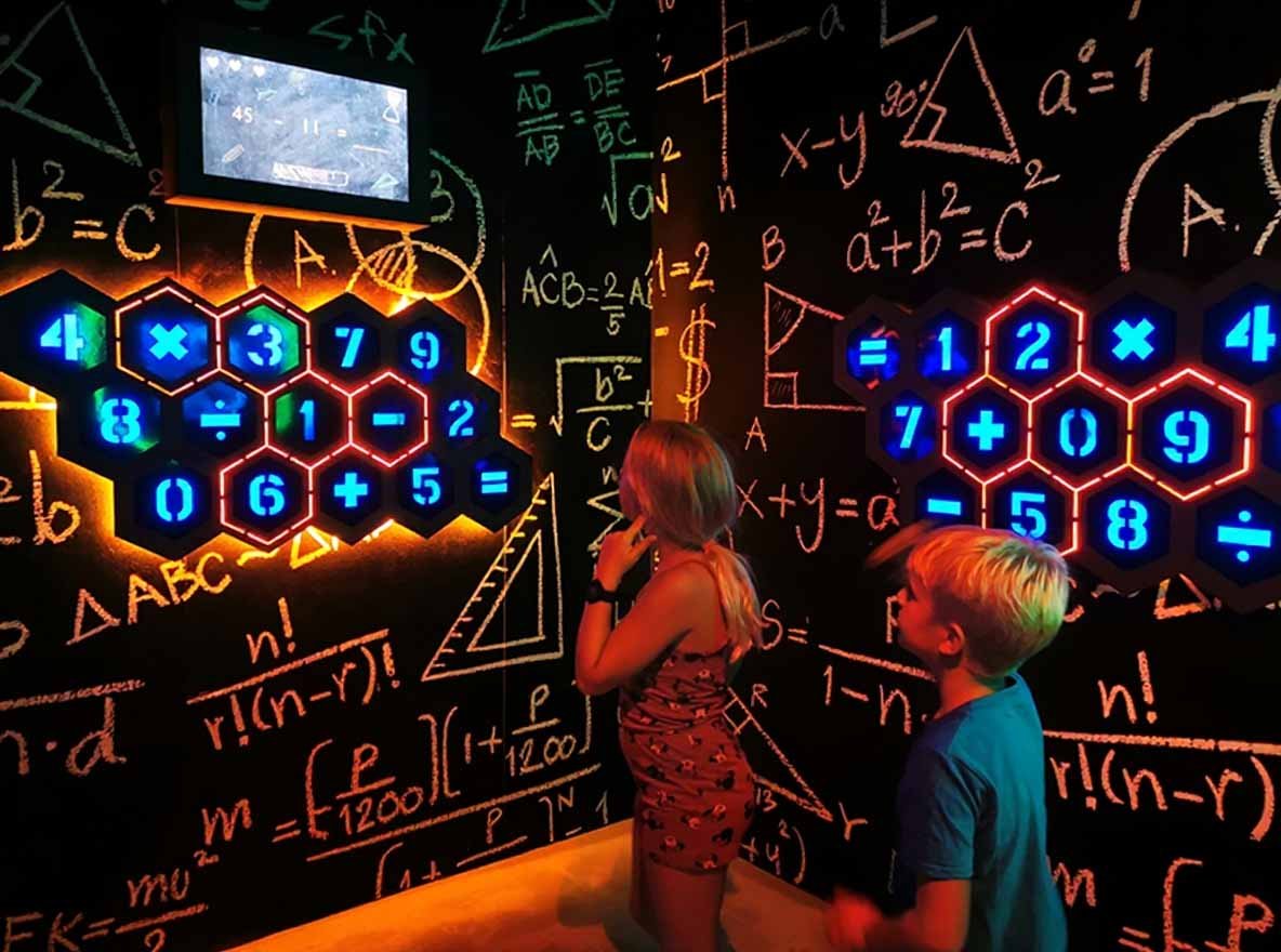 Zwei Kinder spielen das Genius Arithmetic Spiel und wählen die Antwortkombinationen an der Wand basierend auf den Fragen auf dem LED-Bildschirm aus.