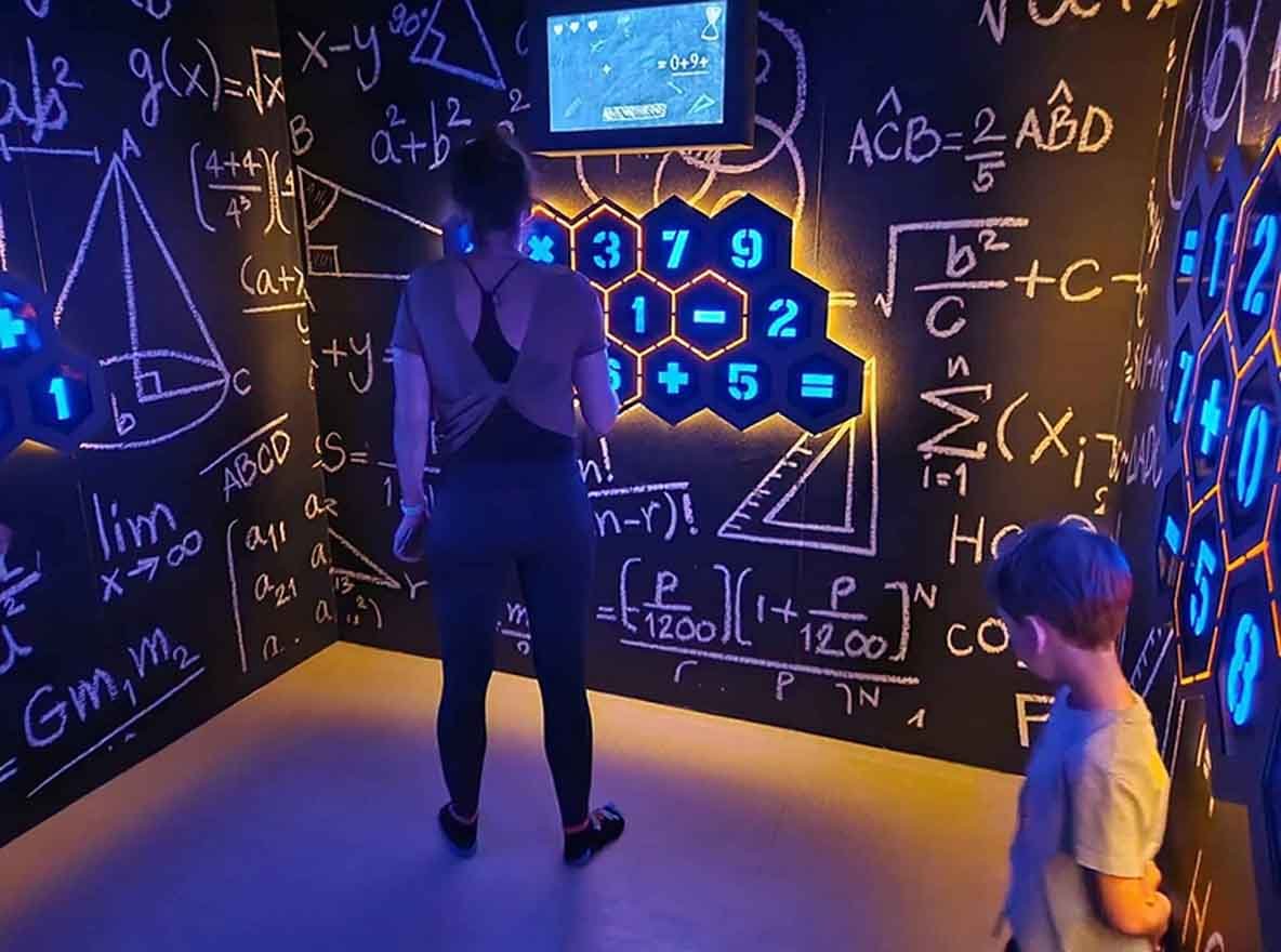 Mutter und Kind spielen Genius Arithmetic und wählen Antworten an der Wand basierend auf den LED-Bildschirmfragen aus.