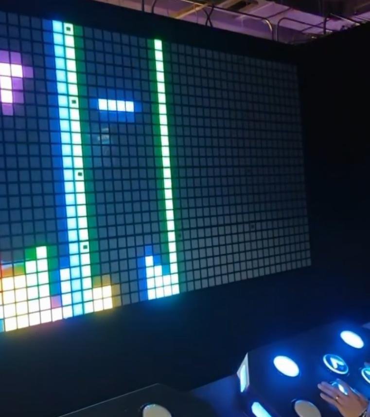 A player using a motion control balance platform to play Tetris on a massive LED pixel screen in an Extreme Control challenge room.
