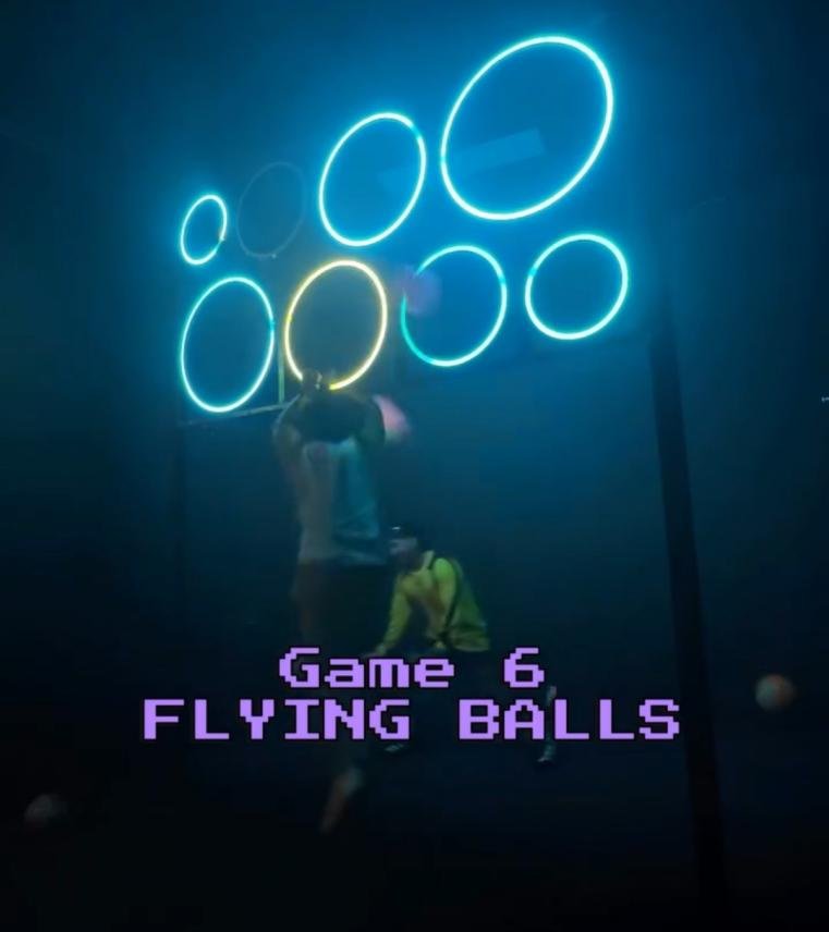 Players throwing balls into glowing neon LED rings in a Flying Balls interactive challenge room.