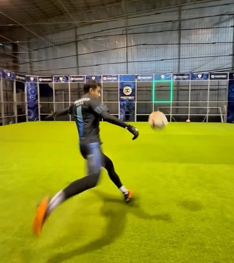 A player kicking a soccer ball toward a moving blue LED target frame in an interactive football challenge game.