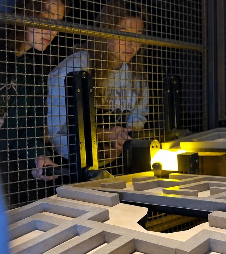Two players working together to tilt and navigate a ball through a balance labyrinth in an Interactive Ball Maze Challenge room.