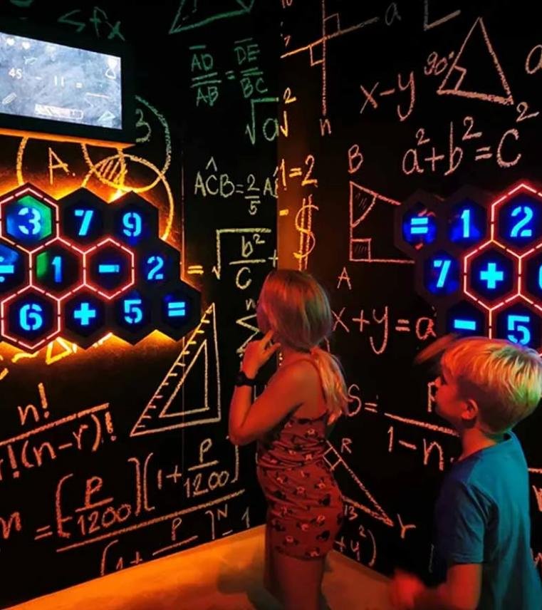 Kids solving fast-paced math puzzles on glowing hexagonal LED panels inside a Math Genius challenge room.